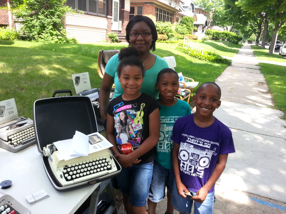 Black family (mother, 2 sons, 1 daughter) standing next to typewriter they have just purchased.