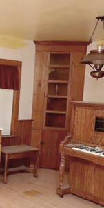 Corner floor-to-ceiling cabinet made of wood. Upper door has 5 glass panes; lower third is a wood door.